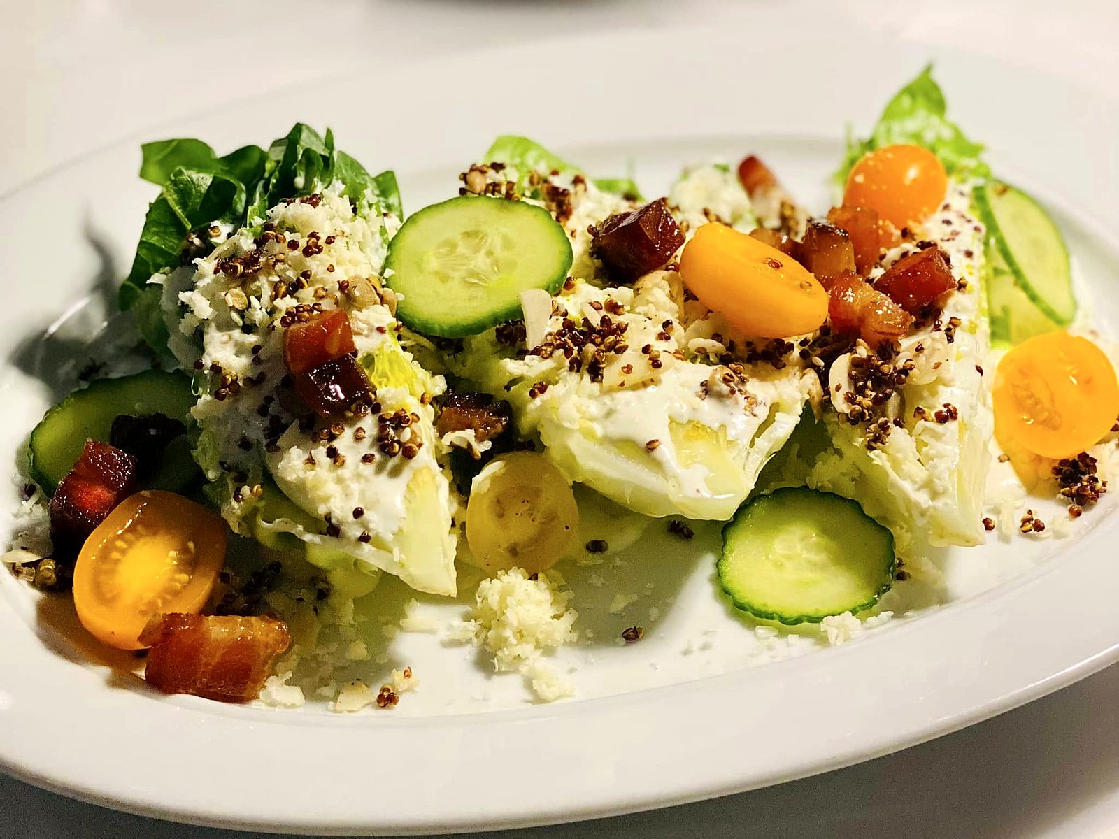 The wedge salad at Verbena — iceberg wedges under buttermilk dressing, shaved cheese, crisped quinoa, bacon lardons, cucumber, and yellow cherry tomatoes.