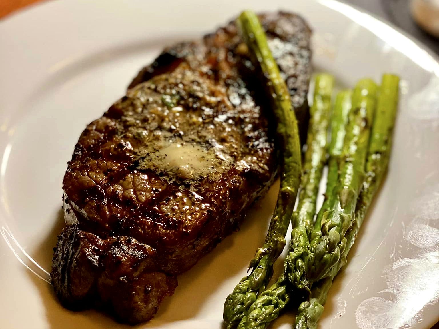 A strip steak at Wilder’s — cross-hatched from the grill, herb butter melting into the crust, grilled asparagus alongside.